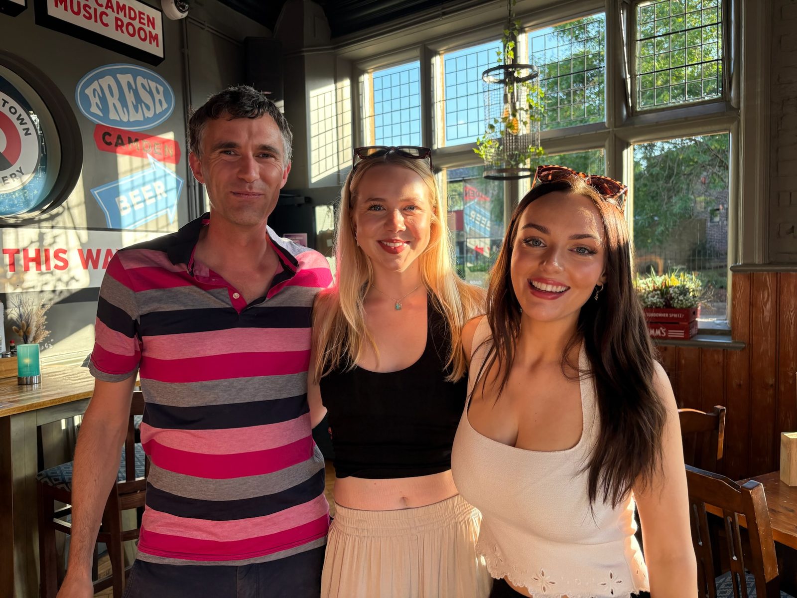 Three people posing together in a sunlit pub