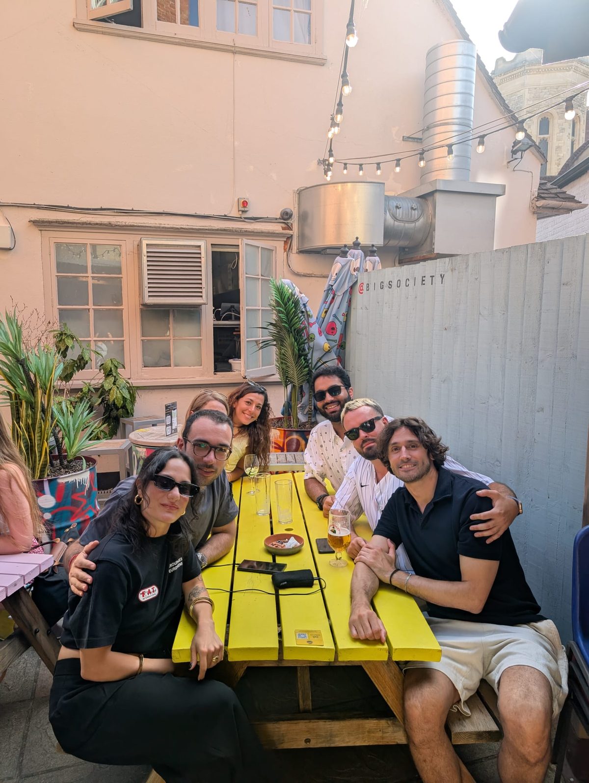 A group sitting together around a bright yellow picnic table in a pub courtyard