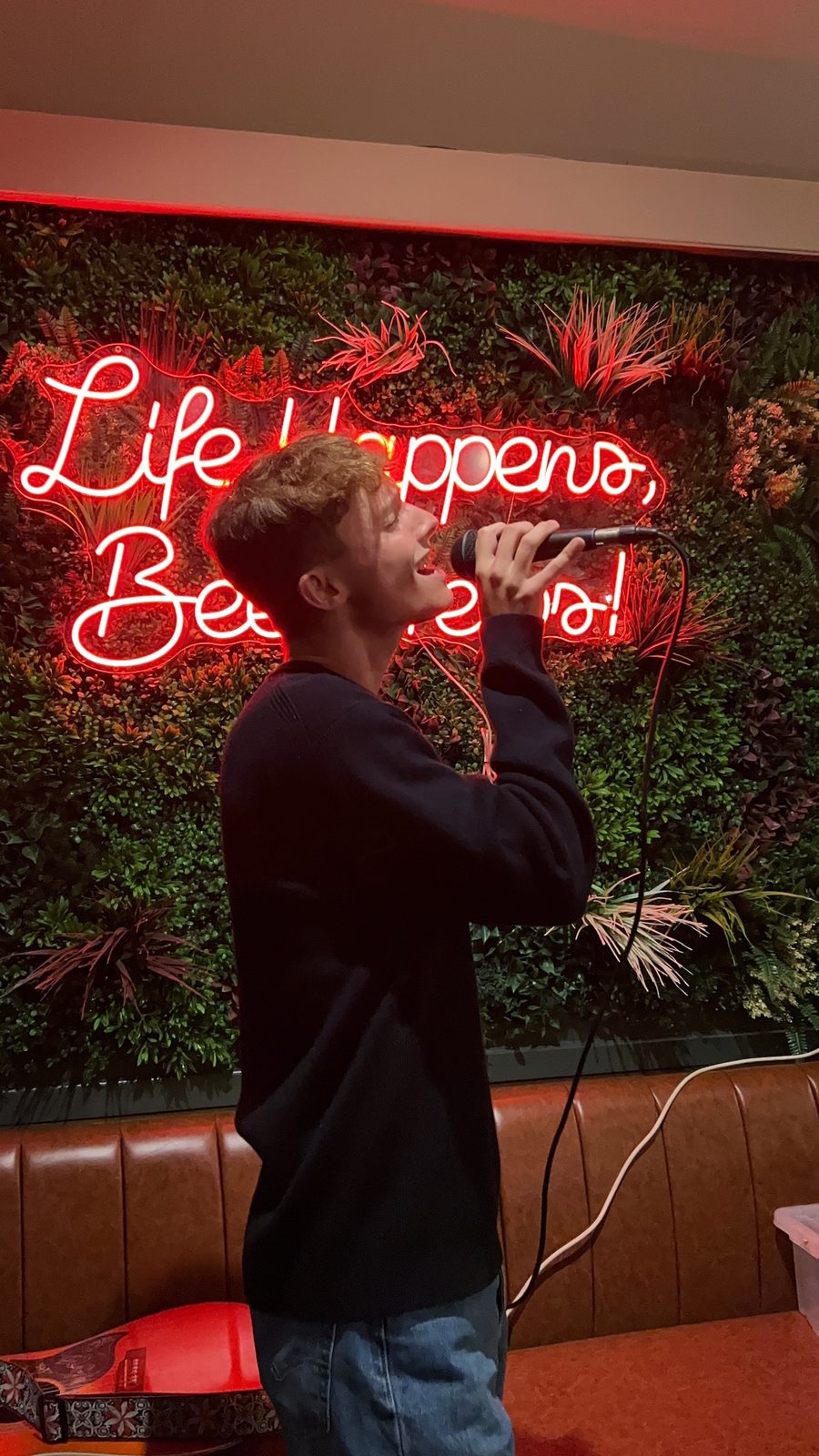 A person singing into a microphone in front of a red neon sign