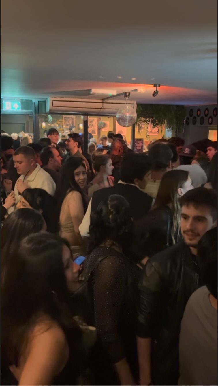 A crowd chatting and dancing beneath a disco ball at Noche Latina!