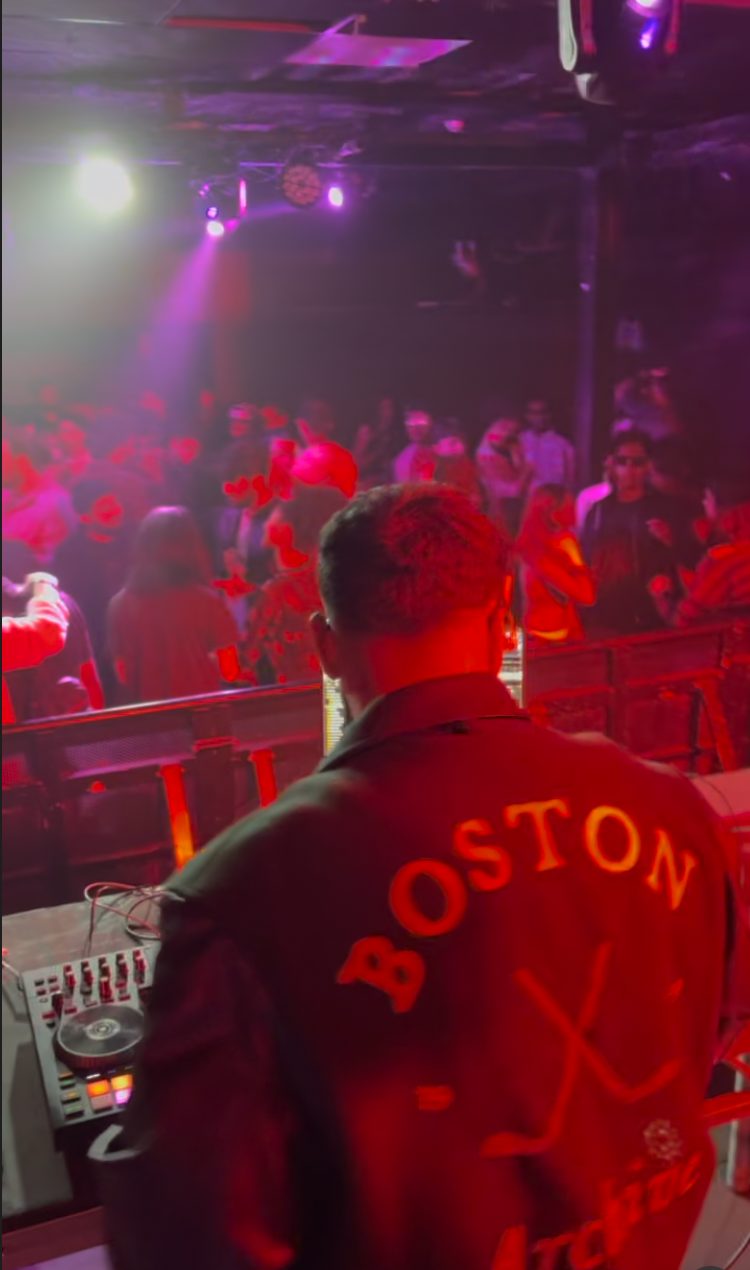 A DJ facing the dance floor under red and purple lights at Bollywood Night