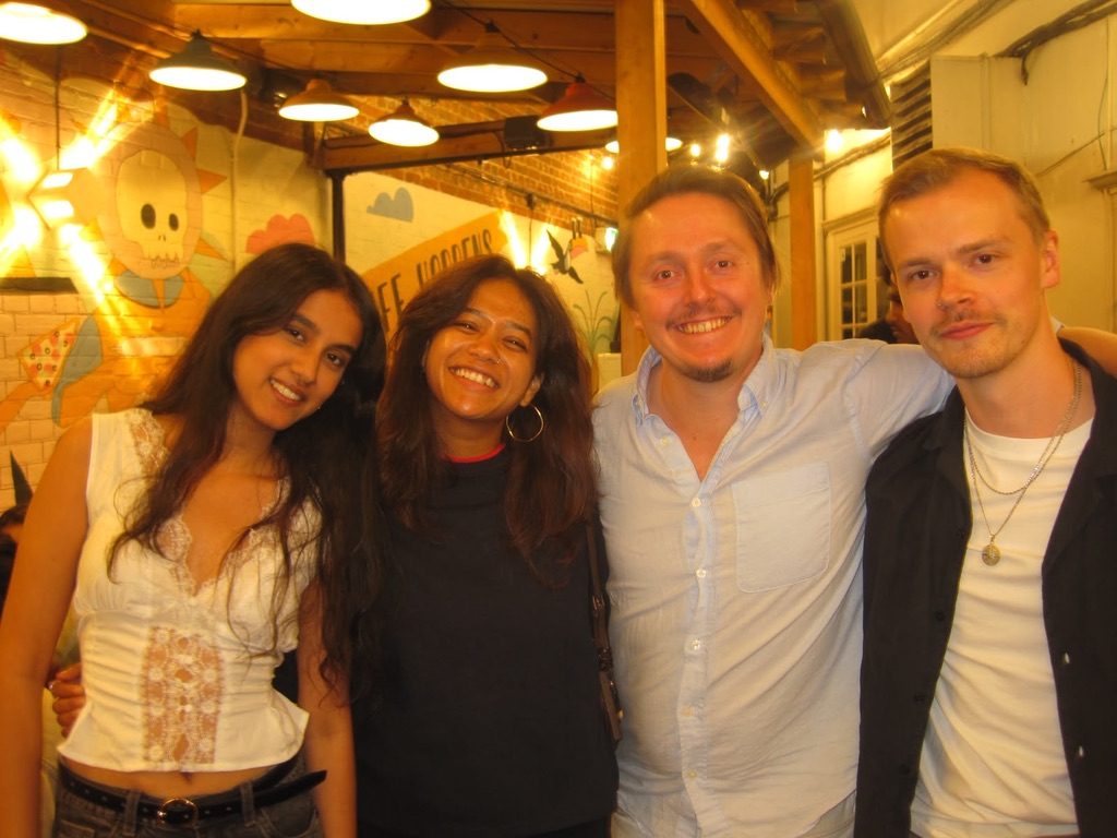 Four people smiling together beneath warm lights in a colourful venue